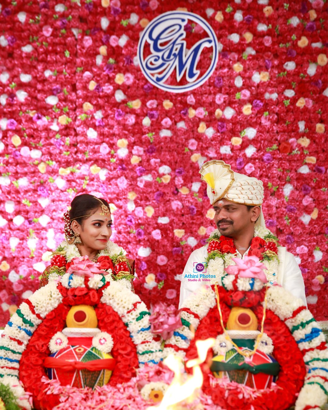A couple posing for a wedding photoshoot, sitting on a red and pink table.