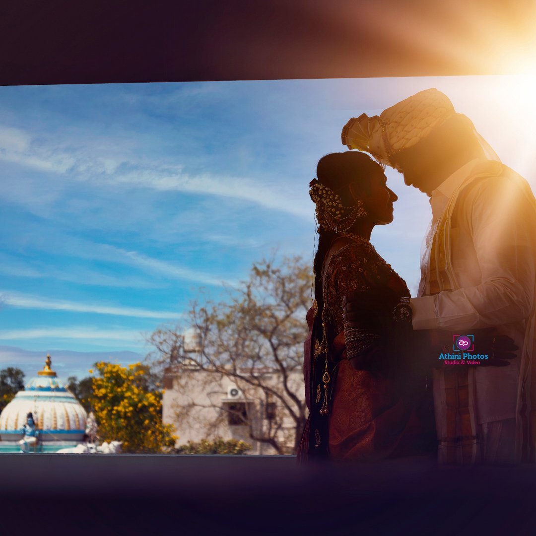 A couple in traditional Indian attire posing for a wedding photoshoot in front of a beautiful building.