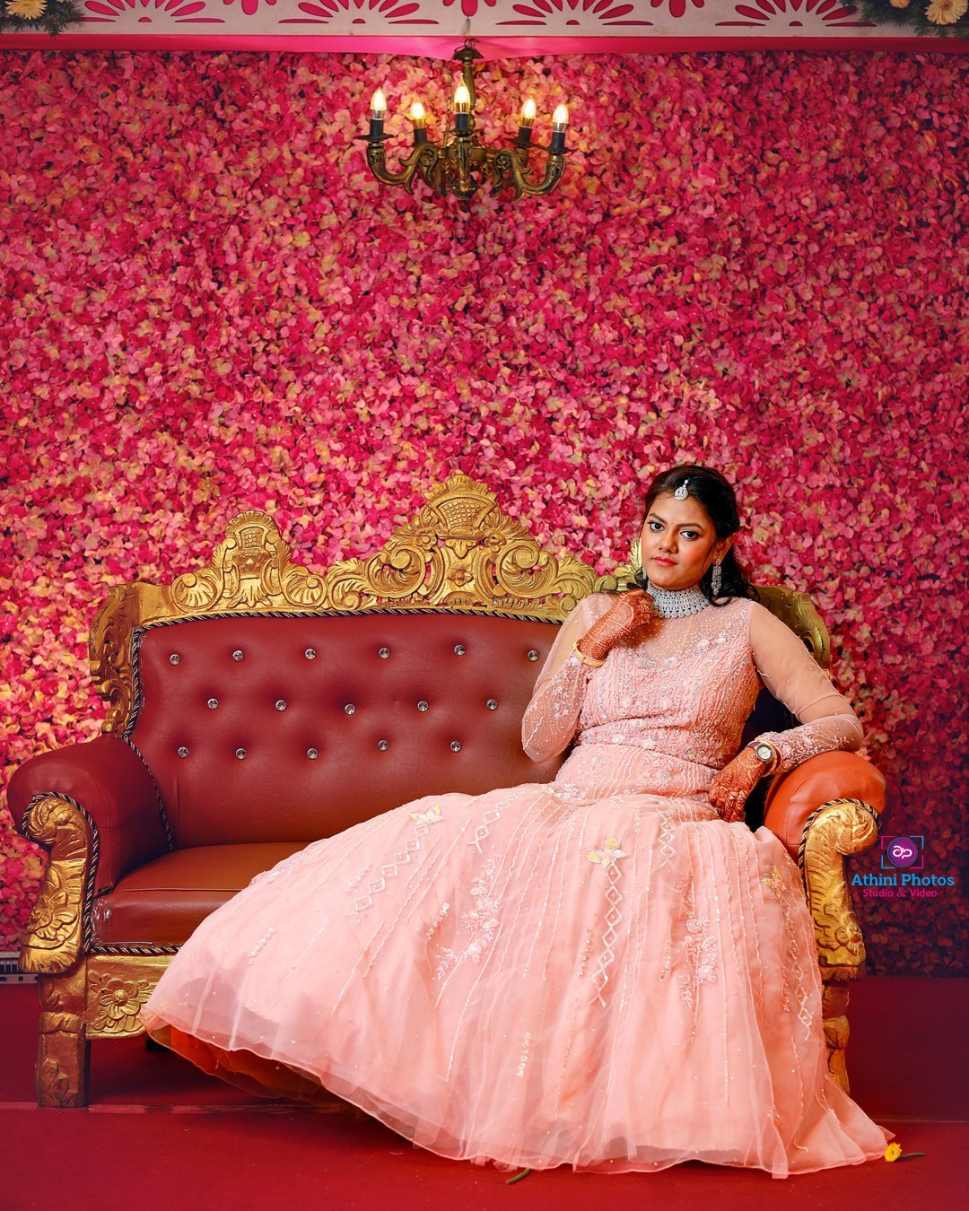 A beautiful bride in a pink gown sitting on a red couch, radiating elegance and grace.