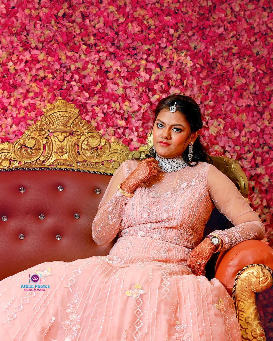 A beautiful bride in a pink gown gracefully sitting on a red couch, radiating elegance and joy.