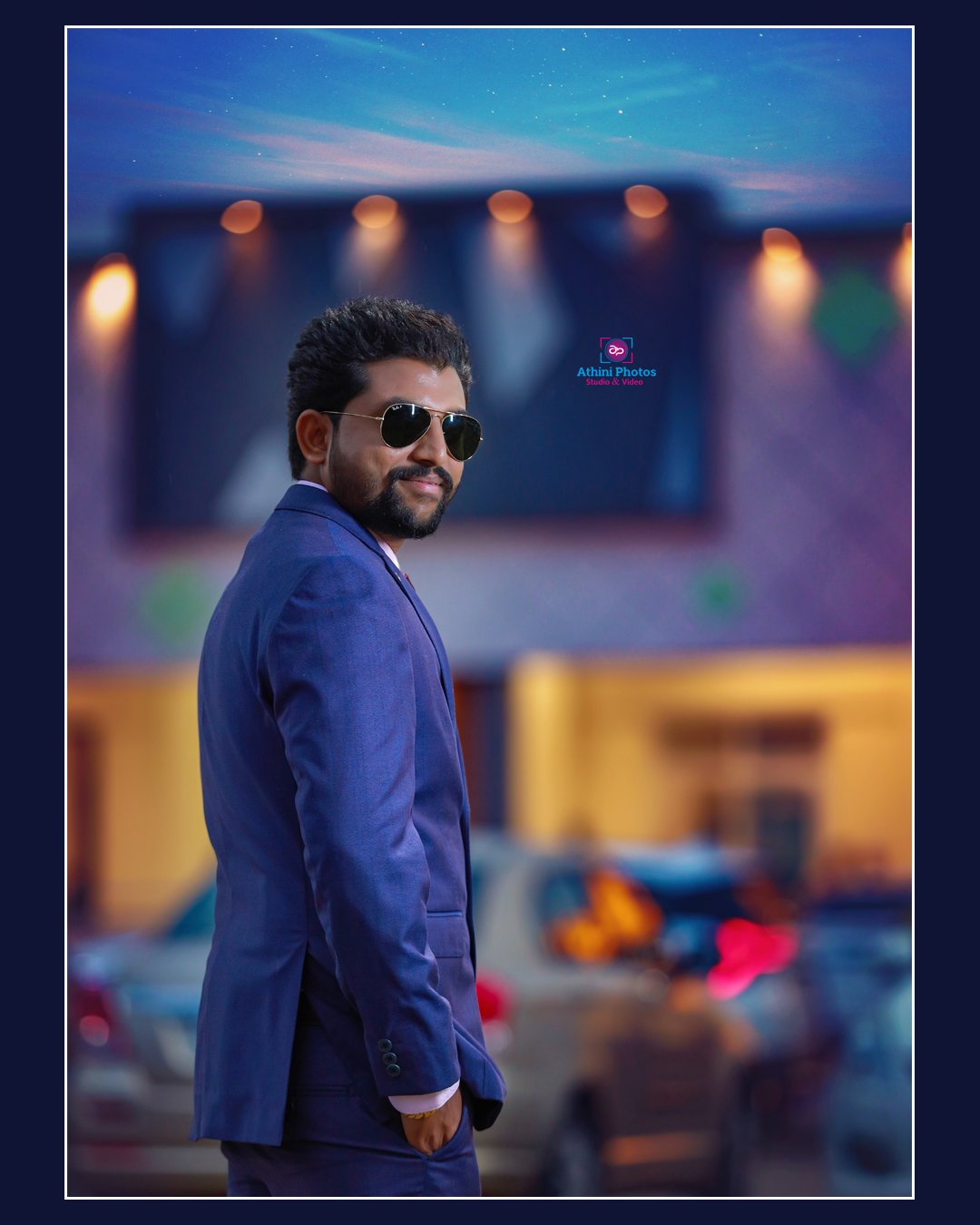 A man in a suit and sunglasses standing confidently in front of a modern office building.