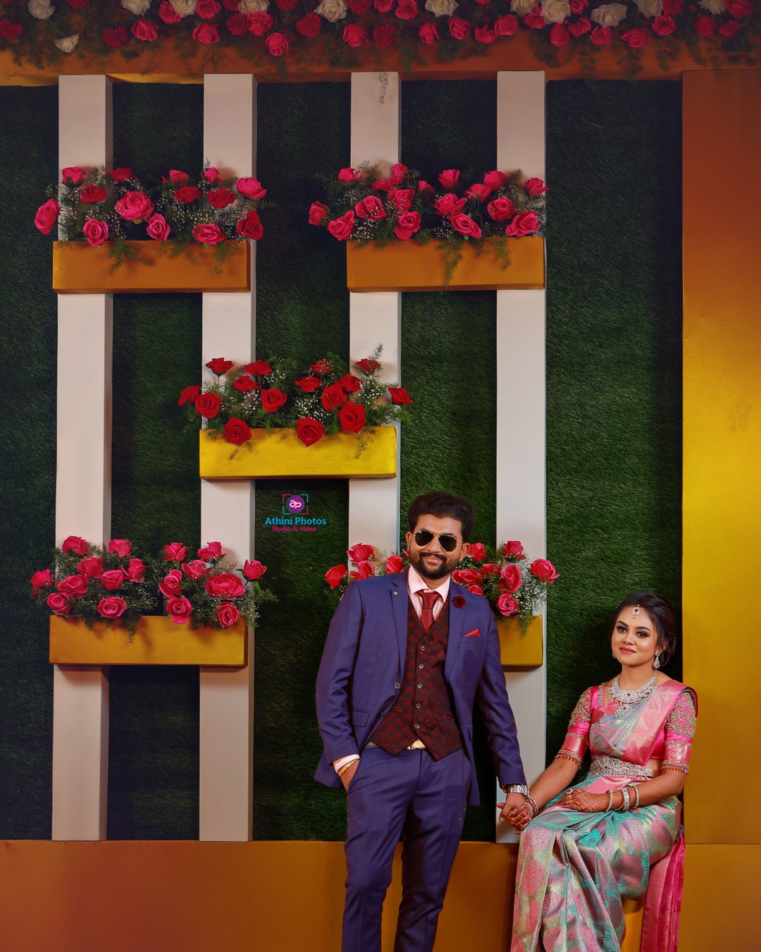 A couple in formal attire posing in front of a flower-adorned wall.